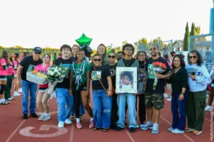 Group of people gathered outdoors, some holding a framed photo and a green balloon.