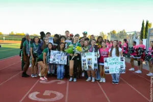 Group of young athletes celebrating on a track field with posters and flowers.