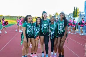 A group of young cheerleaders in green uniforms posing on a track.