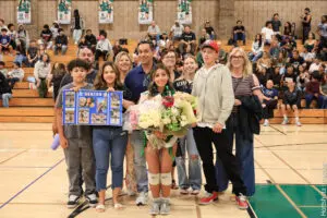 A group photo of a volleyball player with family and friends in a gym.