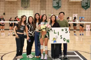 A group of people celebrating a volleyball player with flowers and a supportive sign.