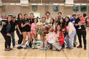 A group of volleyball players and supporters posing with flowers in a gym.