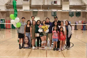 Group photo of smiling people in a gymnasium with balloons and flowers.
