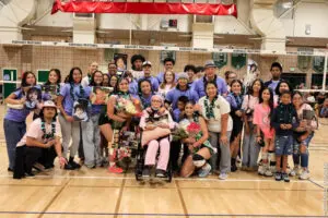 Group photo of diverse people smiling indoors with flowers, including a person in a wheelchair.
