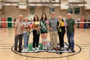 Group of six people standing on a gym floor, holding flowers and trophies.