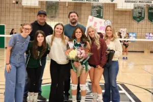 A volleyball player with friends and family celebrating with flowers and a sign.