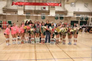 High school girls volleyball team posing with bouquets in gym.