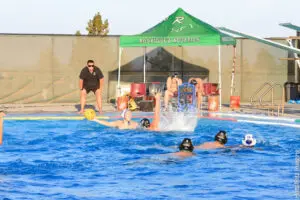 People enjoying a sunny day at a swimming pool with a shaded tent nearby.
