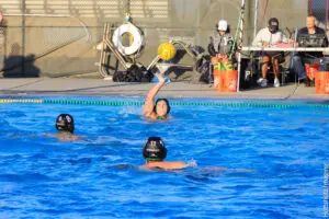 Water polo players compete intensely in a pool, one preparing to shoot.