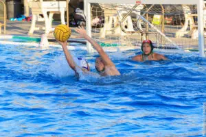 Water polo players compete intensely near the goal in a swimming pool.