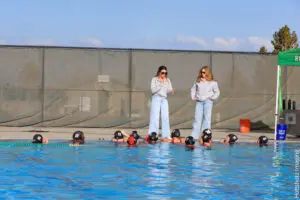 Two instructors teach swimming to a group of children in a pool.