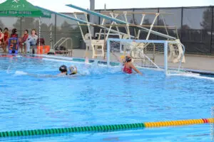 Two children swimming near a water polo goal in a pool.