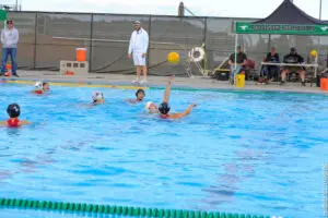 A water polo player reaches for the ball in a pool during a game.