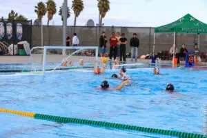 Players compete in a water polo match in an outdoor pool.