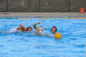Women playing water polo in a pool, fighting for the ball.