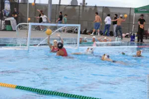 Water polo players compete intensely near the goal in an outdoor pool.
