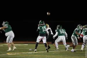 High school football players compete in a night game under stadium lights.