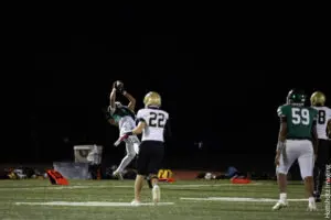 Football player leaps to catch the ball during a night game.