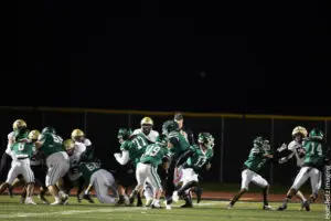 High school football players in action during a night game under stadium lights.