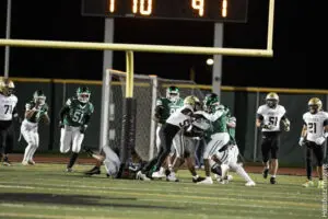 High school football players in green and white uniforms battling near the end zone.
