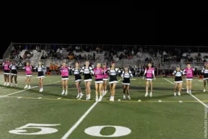 Cheerleaders performing on a football field during a nighttime game.