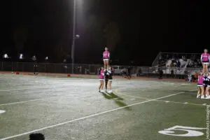 Three cheerleaders performing a stunt on a football field at night.