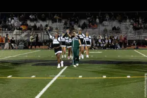 Cheerleaders performing on a football field at night with spectators.