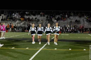 Four cheerleaders performing on a football field at night.