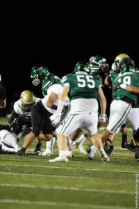 High school football players in green and white uniforms competing on the field.