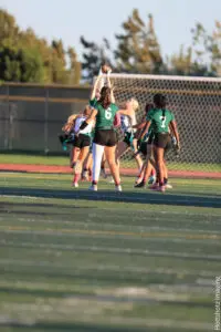 Girls playing field hockey on an outdoor turf field during the day.