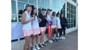 A group of women golfers posing with a trophy outside a building.