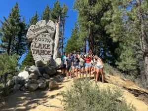 Group of people posing by South Lake Tahoe sign in a forested area.