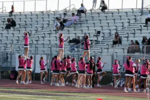 Cheerleaders in pink uniforms preparing on stadium bleachers.