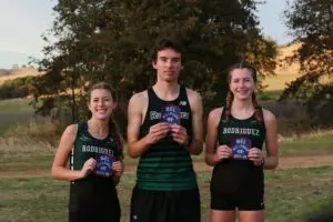 Three young athletes holding awards outdoors in sportswear.
