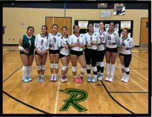 A girls volleyball team posing in a gym.