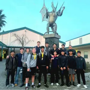 A group of young people posing in front of a knight statue outdoors.