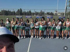 A girls' field hockey team posing on the field with their coach.