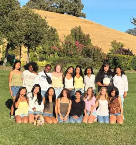 A group of young women posing outdoors on a sunny day.