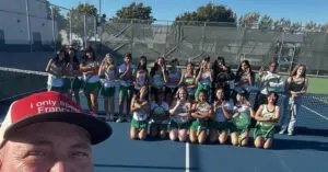A group of young girls in sports uniforms posing on a tennis court.