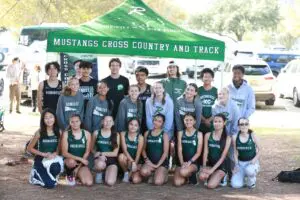 High school cross country team posing outdoors in uniforms under a green team tent.