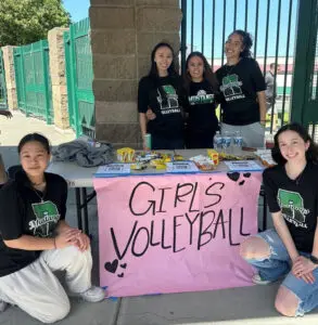 Girls' volleyball team posing with a decorated sign.