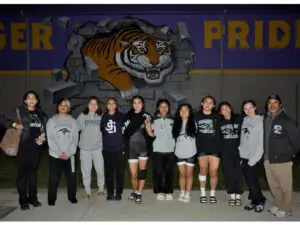 A group of young women posing in front of a tiger mural at night.