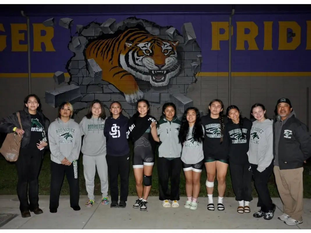 A group of young women posing in front of a tiger mural at night.