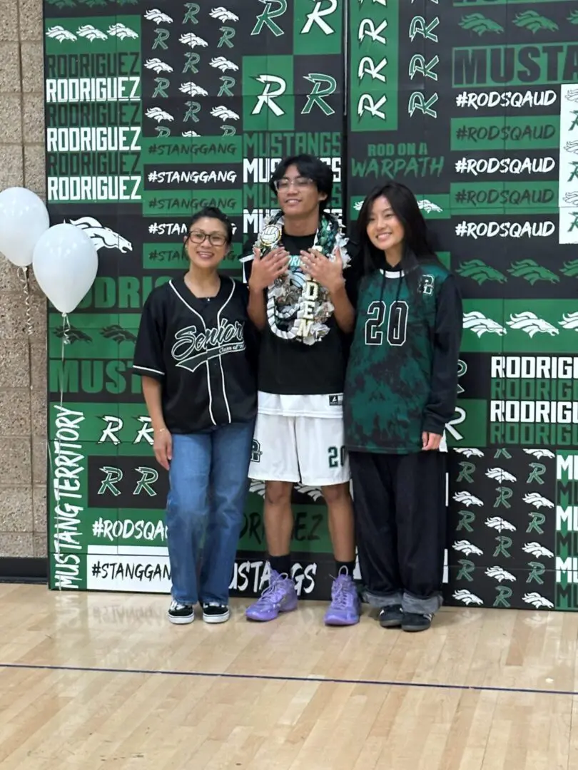 Three people posing at high school sports backdrop
