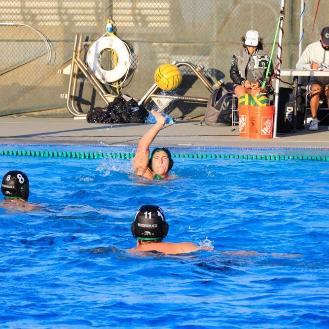 Water polo players compete intensely in a pool, one preparing to shoot.