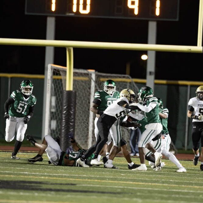High school football players in green and white uniforms battling near the end zone.