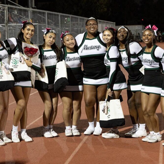 A group of seven cheerleaders posing on a track at night.