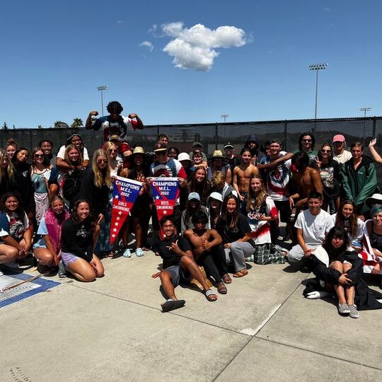 Large group of diverse people posing outdoors on a sunny day.