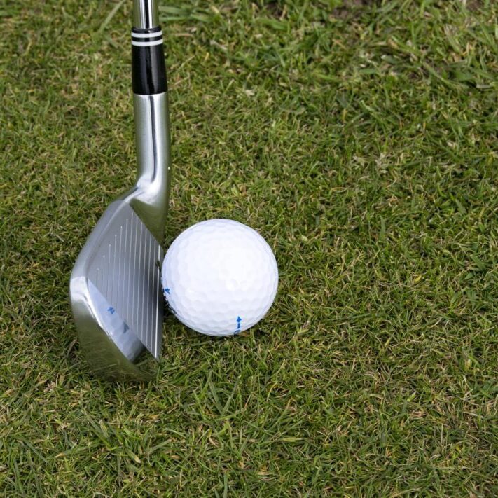 Golf club positioned next to a golf ball on green grass.