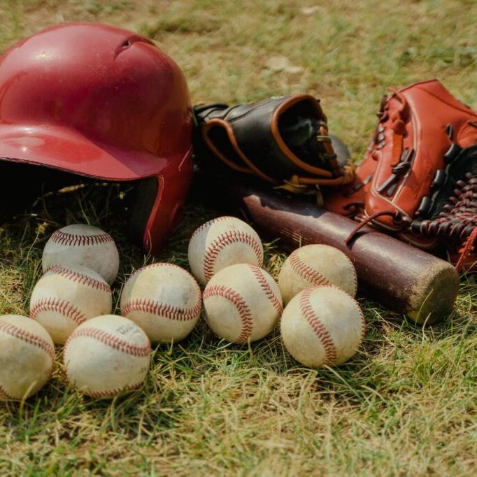 Baseball gear including helmet, gloves, bat, and balls on grass.